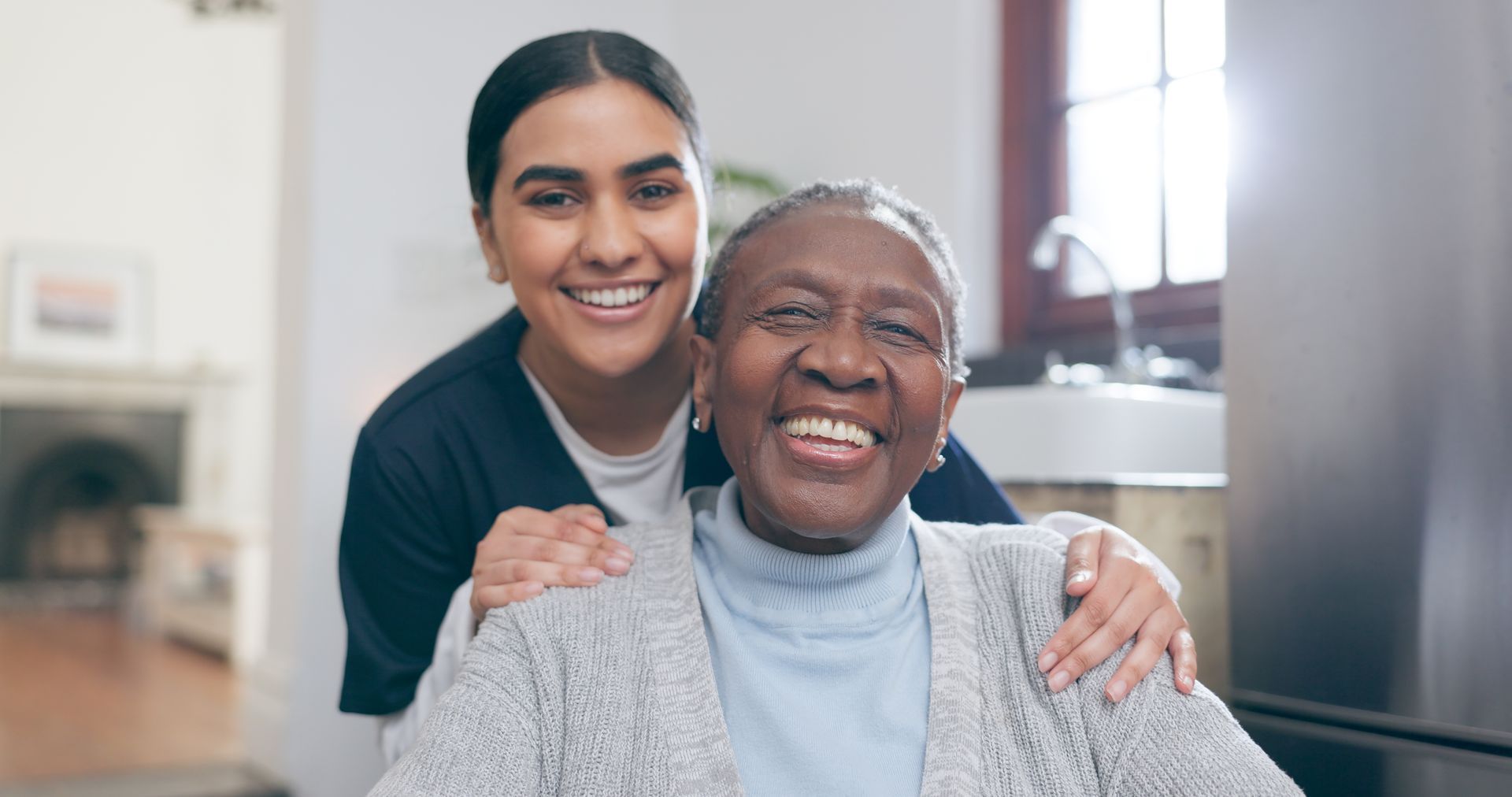 Une femme souriante enlace une personne âgée dans un salon lumineux.