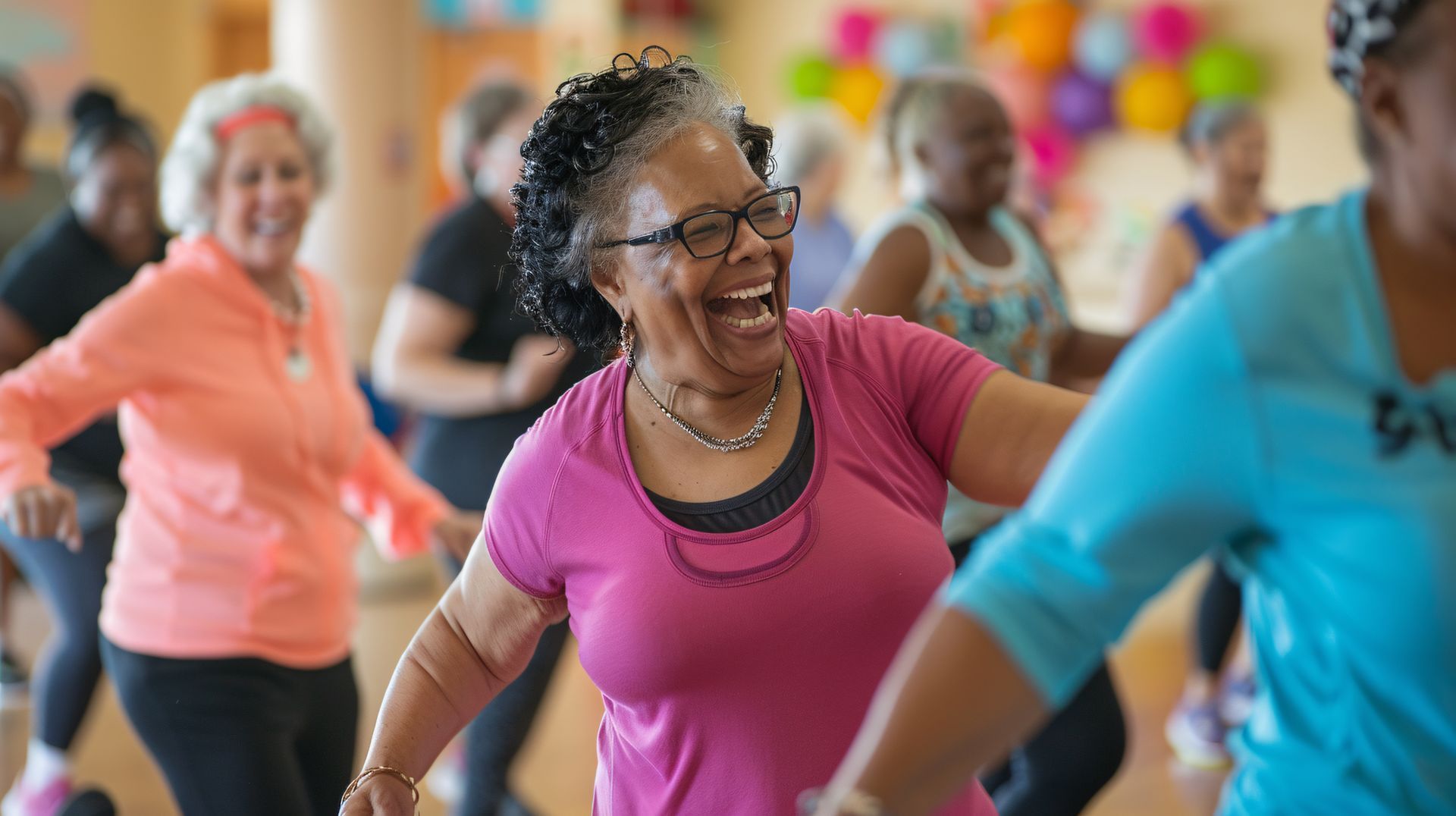 Des personnes souriantes et en mouvement, vêtues de tenues colorées font du sport dans un cours de fitness lumineux.