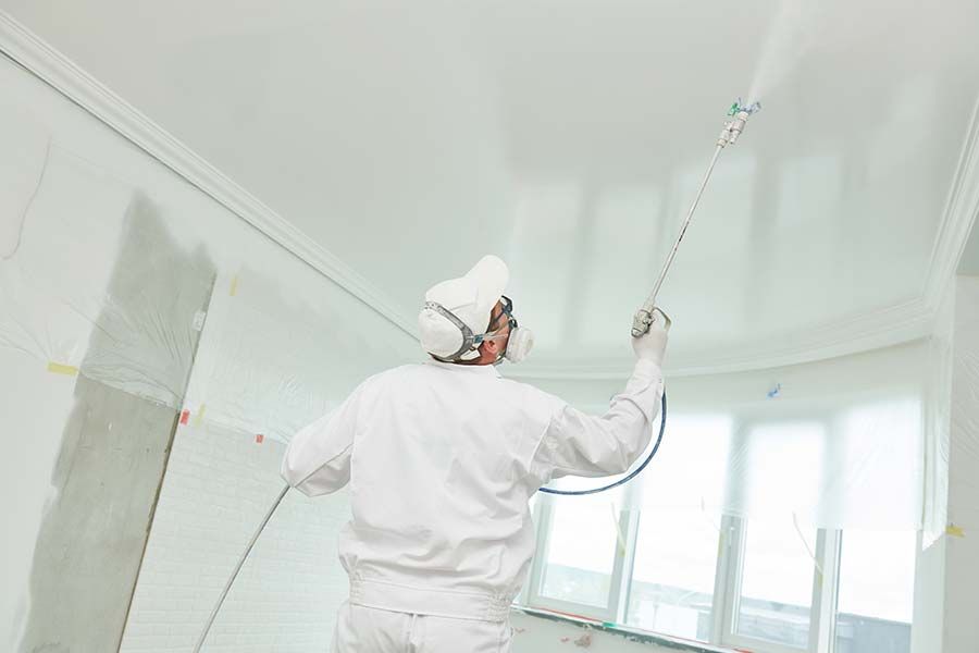 Un homme en train de peindre un plafond par projection sans air