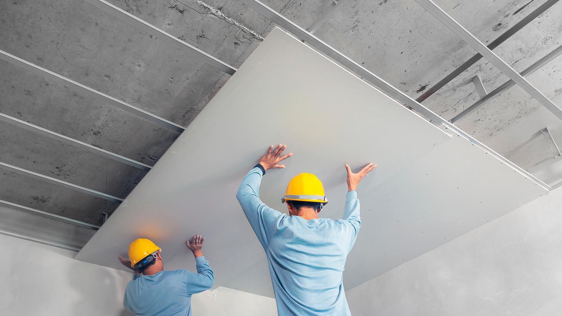 Deux hommes appliquent une plaque de plâtre à la structure du plafond