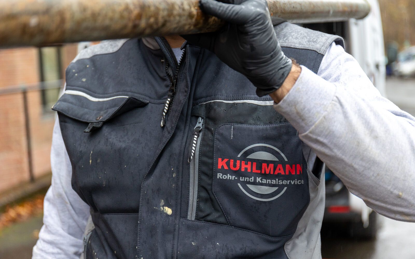 Ein Mann mit einer Kuhlmann Rohr- und Kanalservice-Weste trägt ein Rohr auf seiner Schulter.