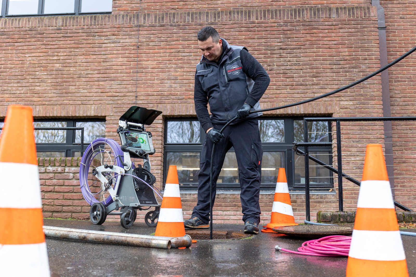 Ein Mann arbeitet an einem Kanaldeckel vor einem Backsteingebäude.