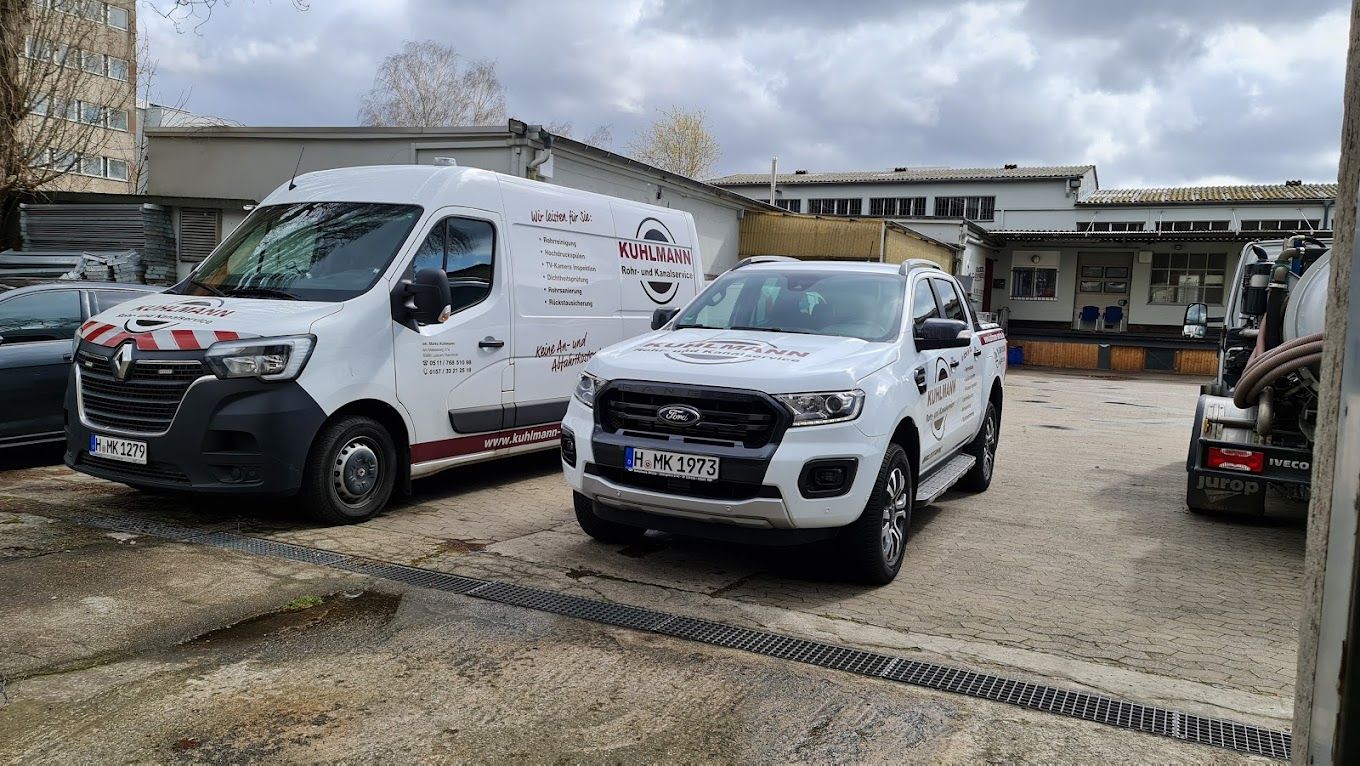 Zwei weiße Lastwagen und ein weißer Lieferwagen parken vor einem Gebäude.