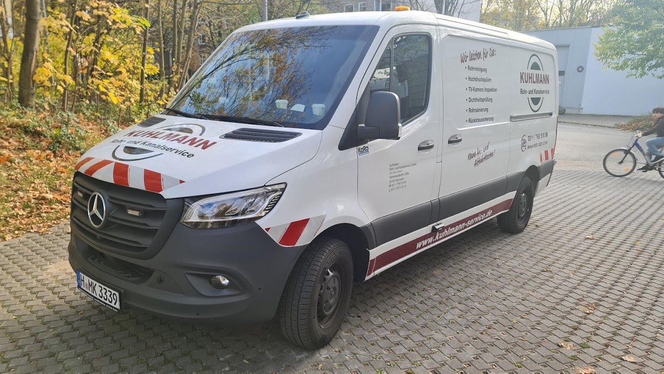 Ein weißer Lieferwagen steht neben einem Fahrrad auf einer gepflasterten Auffahrt.