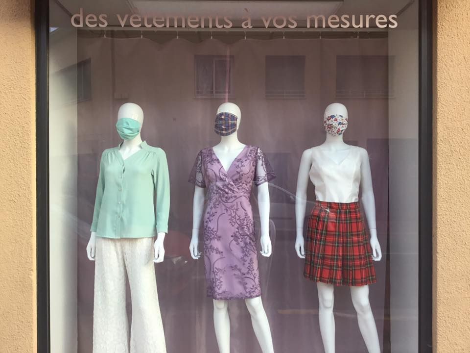 Vitrine de boutique présentant des mannequins habillés de tenues variées, incluant un tailleur pastel et une jupe à carreaux.