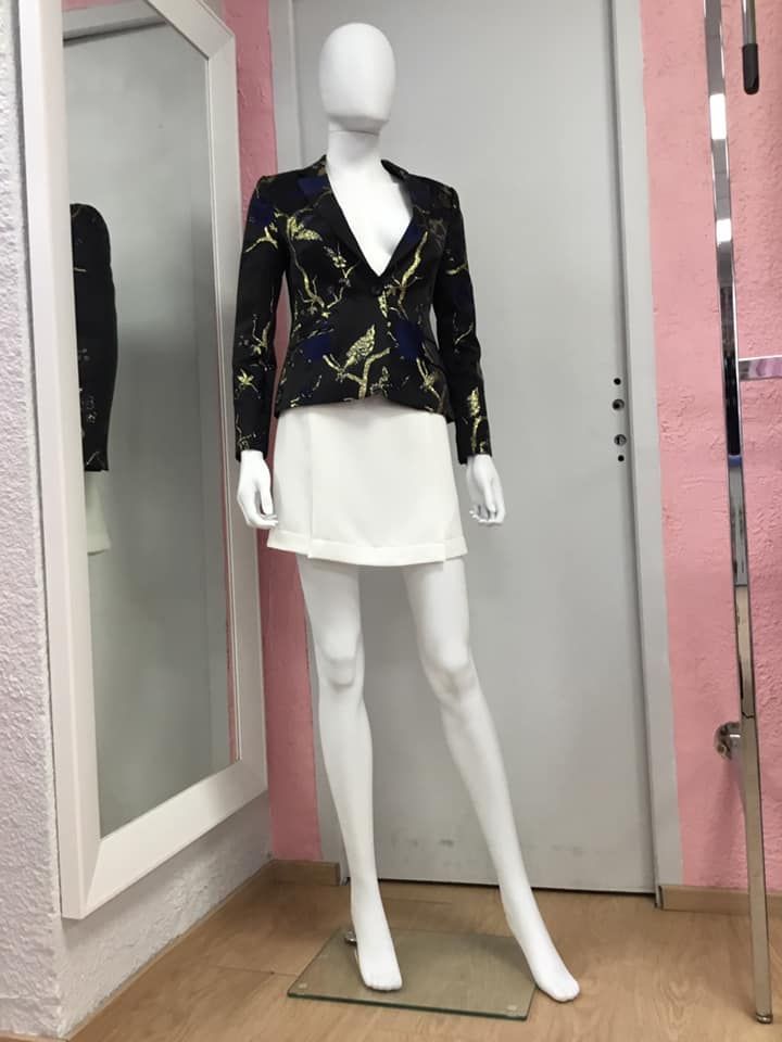 Blazer noir fermée à motifs dorés porté sur une tunique blanche 