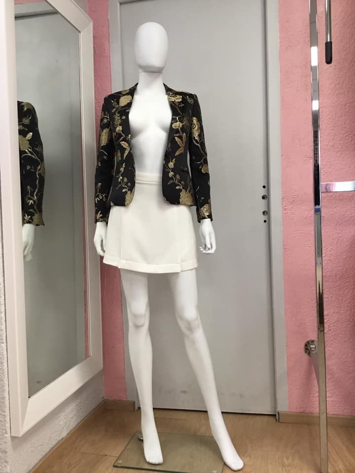 Blazer noir à motifs dorés accompagné d'une jupe blanche