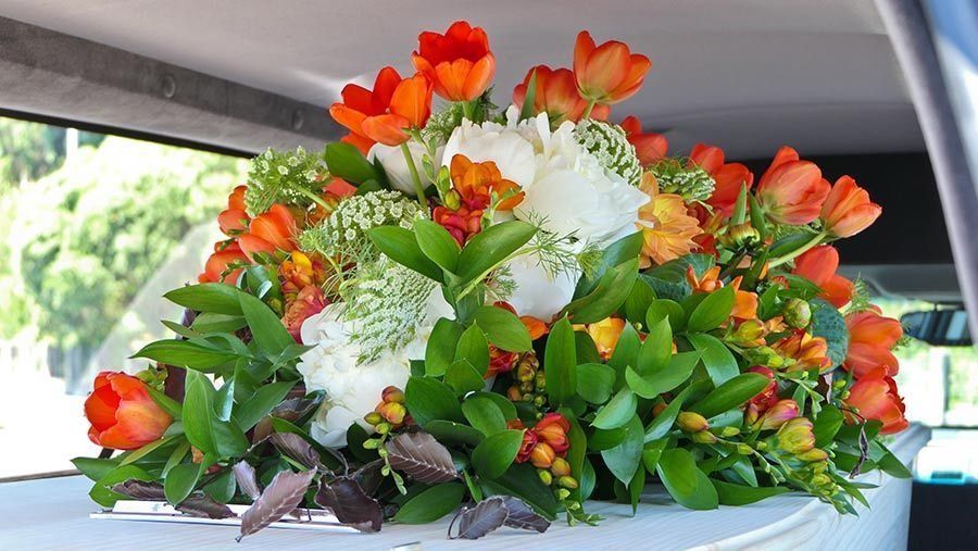 Un ataúd blanco con flores naranjas y blancas encima.