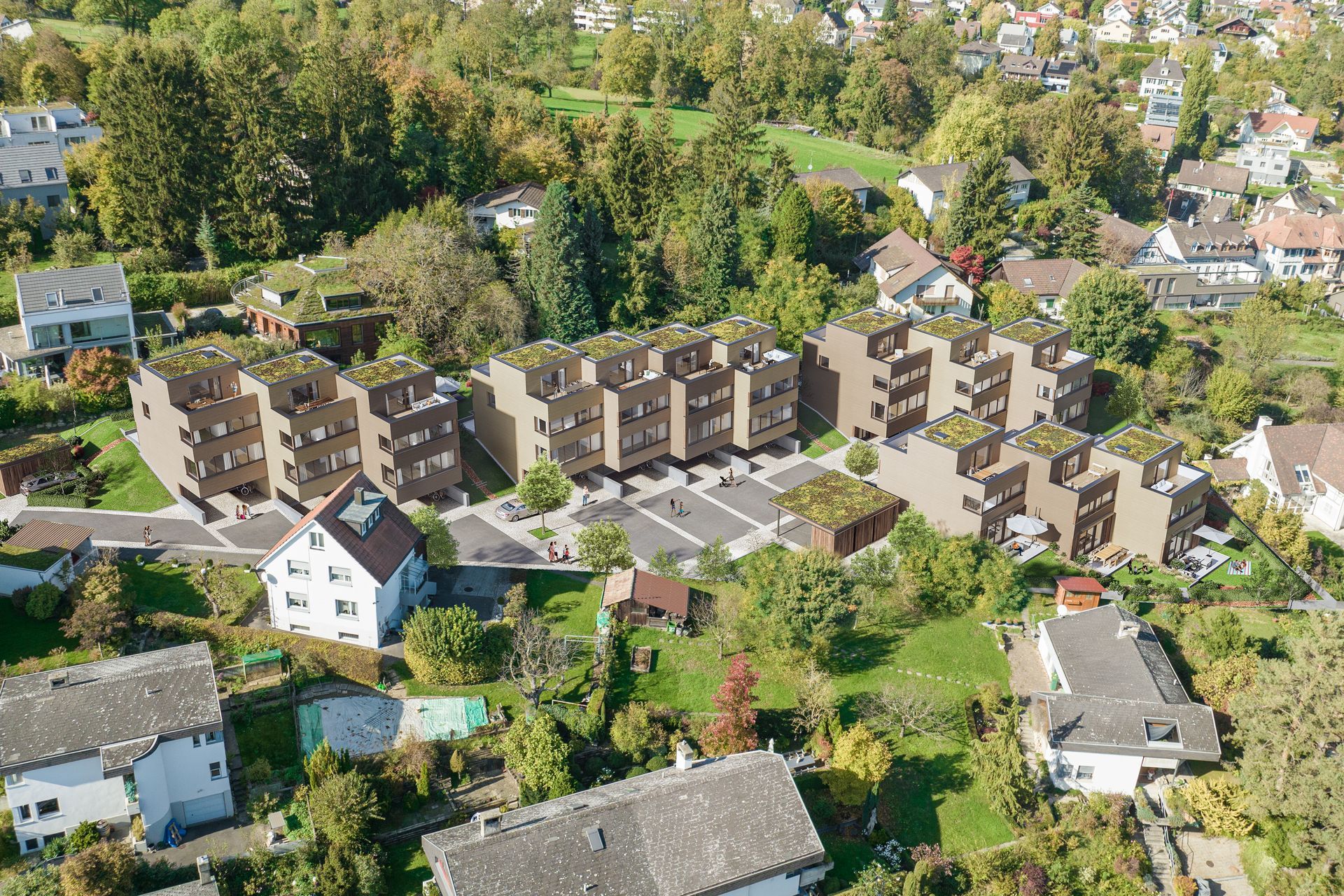 Luftaufnahme eines neuen Wohnkomplexes mit braun getönten Reihenhäusern und Gründächern, umgeben von Bäumen.