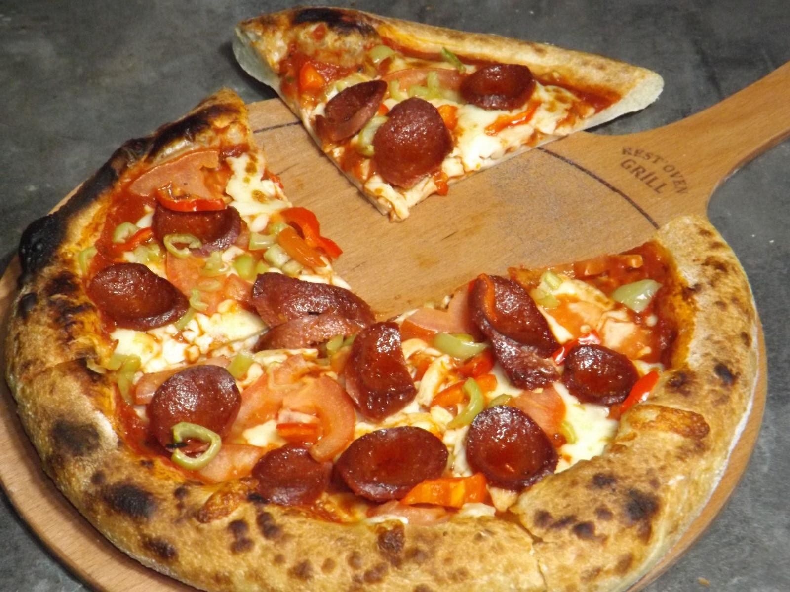 Une pizza pepperoni sur une pelle à pizza en bois, une part retirée.