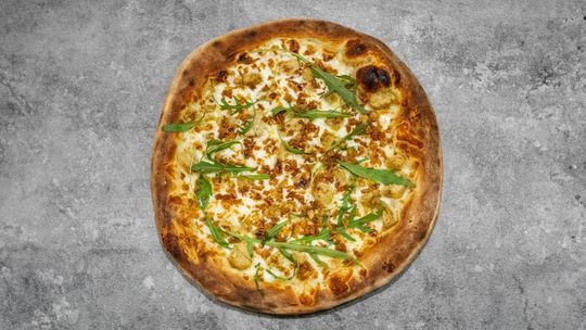 Une pizza ronde garnie de fromage fondu, de petits morceaux dorés et de roquette fraîche éparpillée, posée sur une surface grise texturée.
