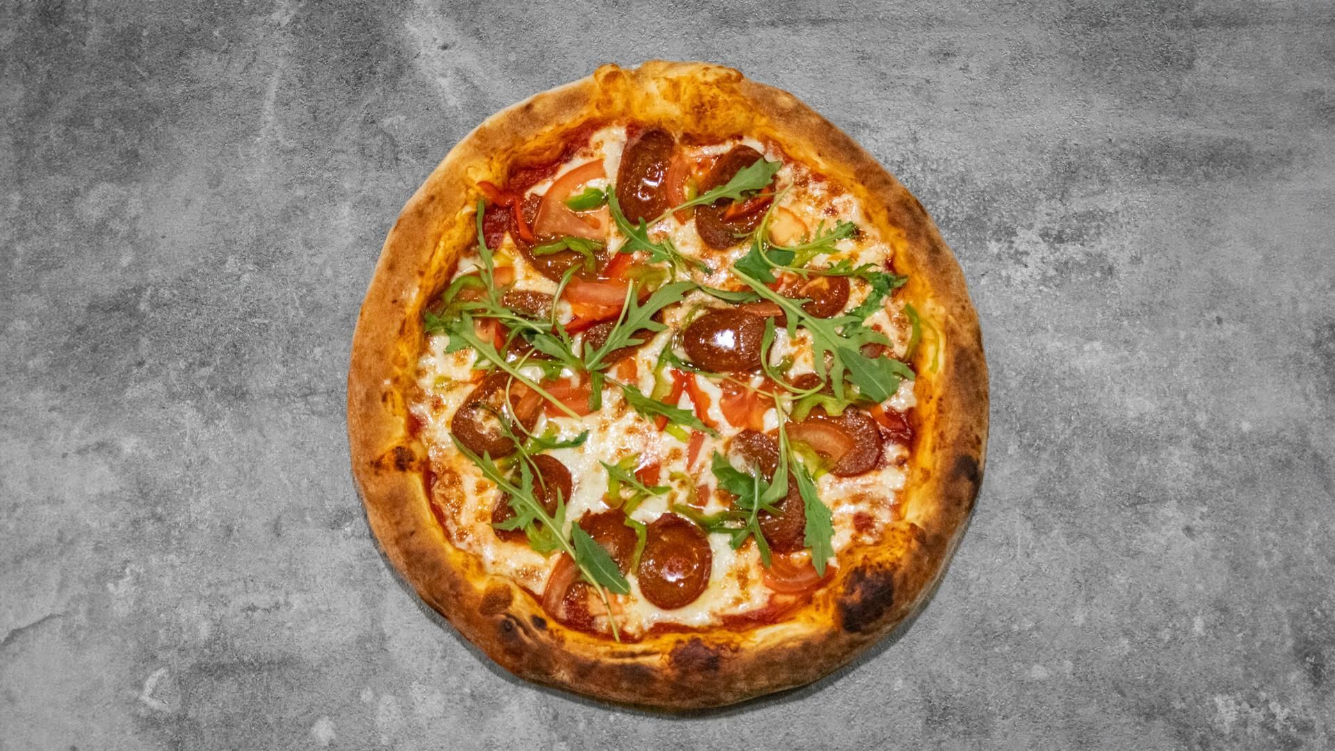 Une pizza ronde garnie de pepperoni, de fromage fondu, de sauce tomate et de roquette fraîche sur une pâte grise.
