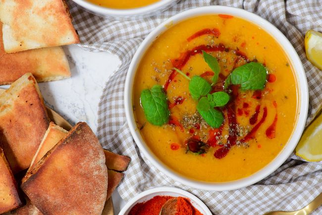 Un bol de soupe de lentilles dorées garnie de menthe et d'huile pimentée, servie avec du pain pita grillé et des quartiers de citron.