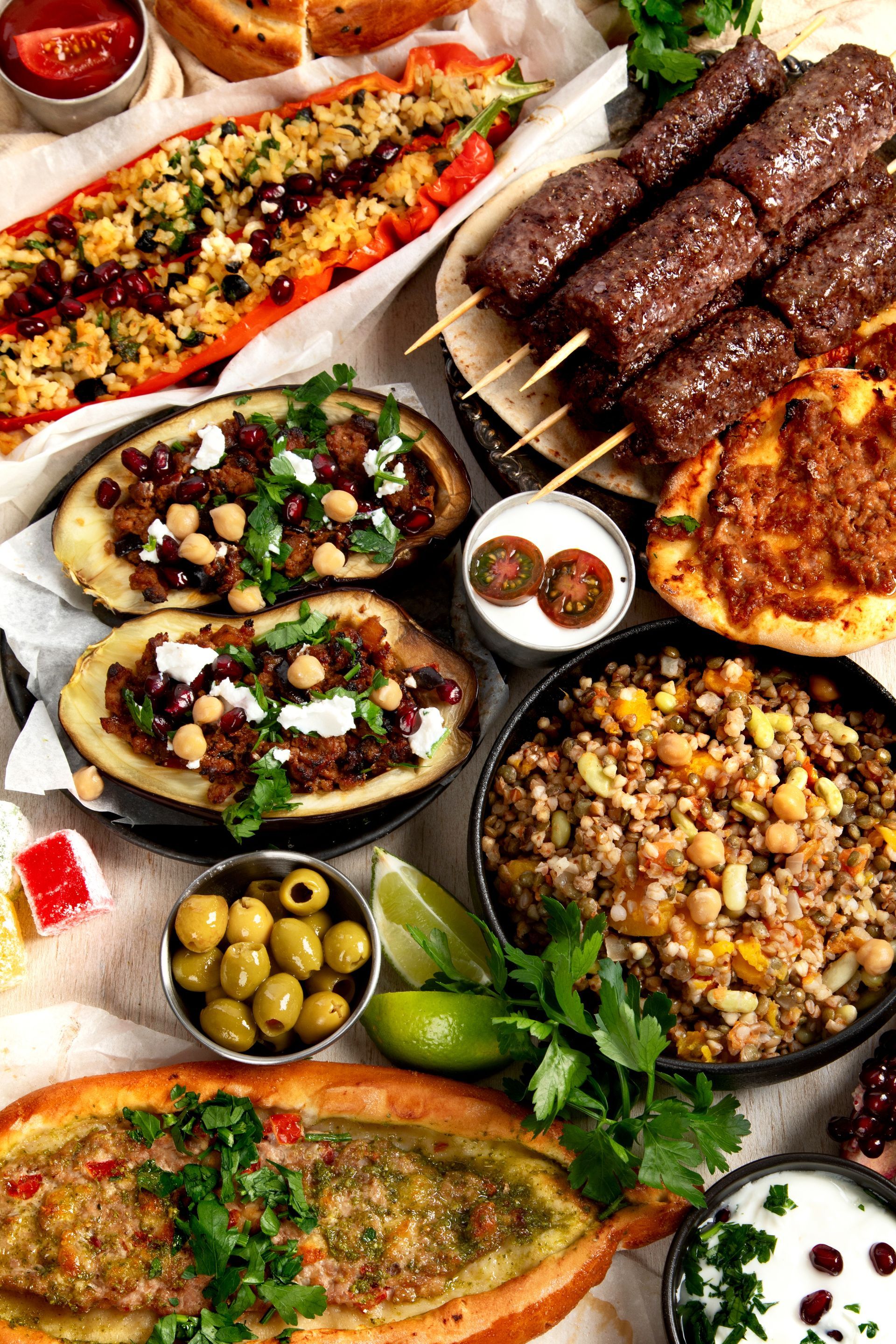 Un assortiment de plats méditerranéens, comprenant des brochettes grillées, des pains plats farcis, des aubergines rôties, des olives et des salades de céréales.