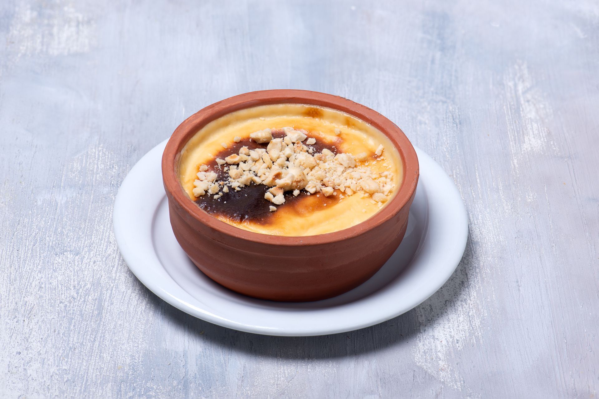Un bol en terre cuite contenant du riz au lait garni d'amandes concassées, servi sur une assiette blanche sur fond gris clair.