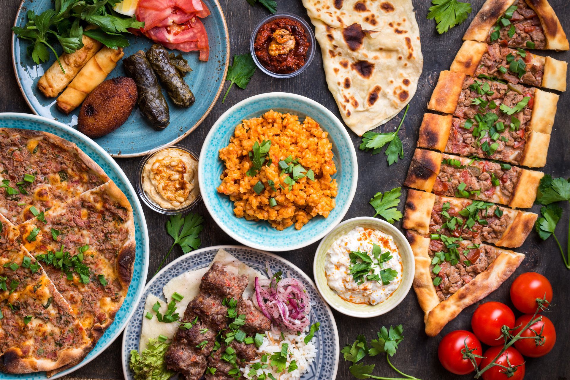 Vue plongeante d'un festin turc composé de lahmacun, de pide, de feuilles de vigne farcies, de riz et de sauces sur une table sombre.