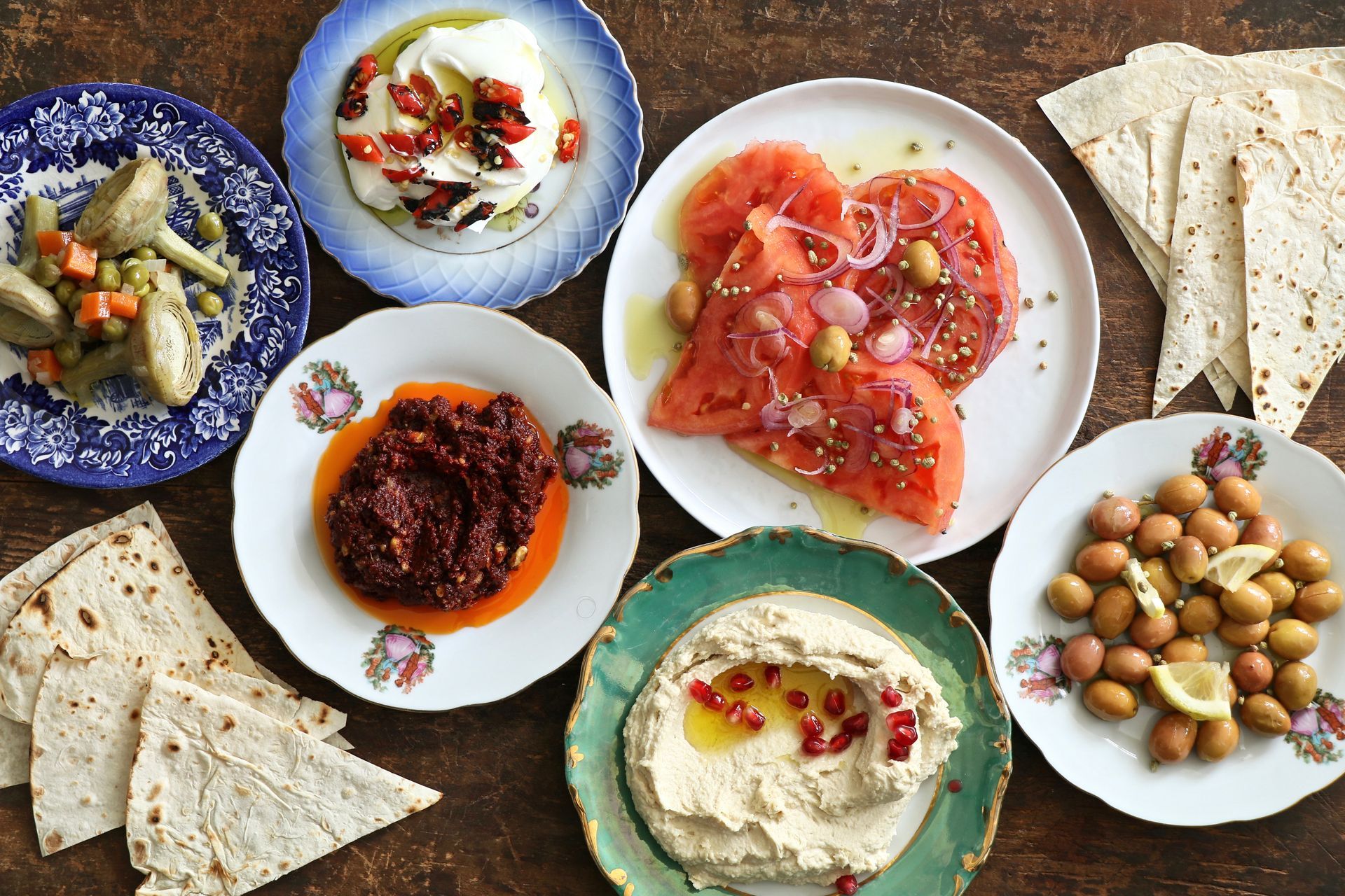 Une table garnie de mezze méditerranéens, comprenant du houmous, des olives, de la salade de tomates, des sauces et des pains plats.