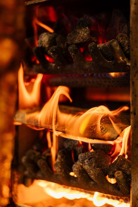 Une cheminée à plusieurs niveaux avec des braises incandescentes et des flammes orange vif qui s'élèvent entre les grilles métalliques.