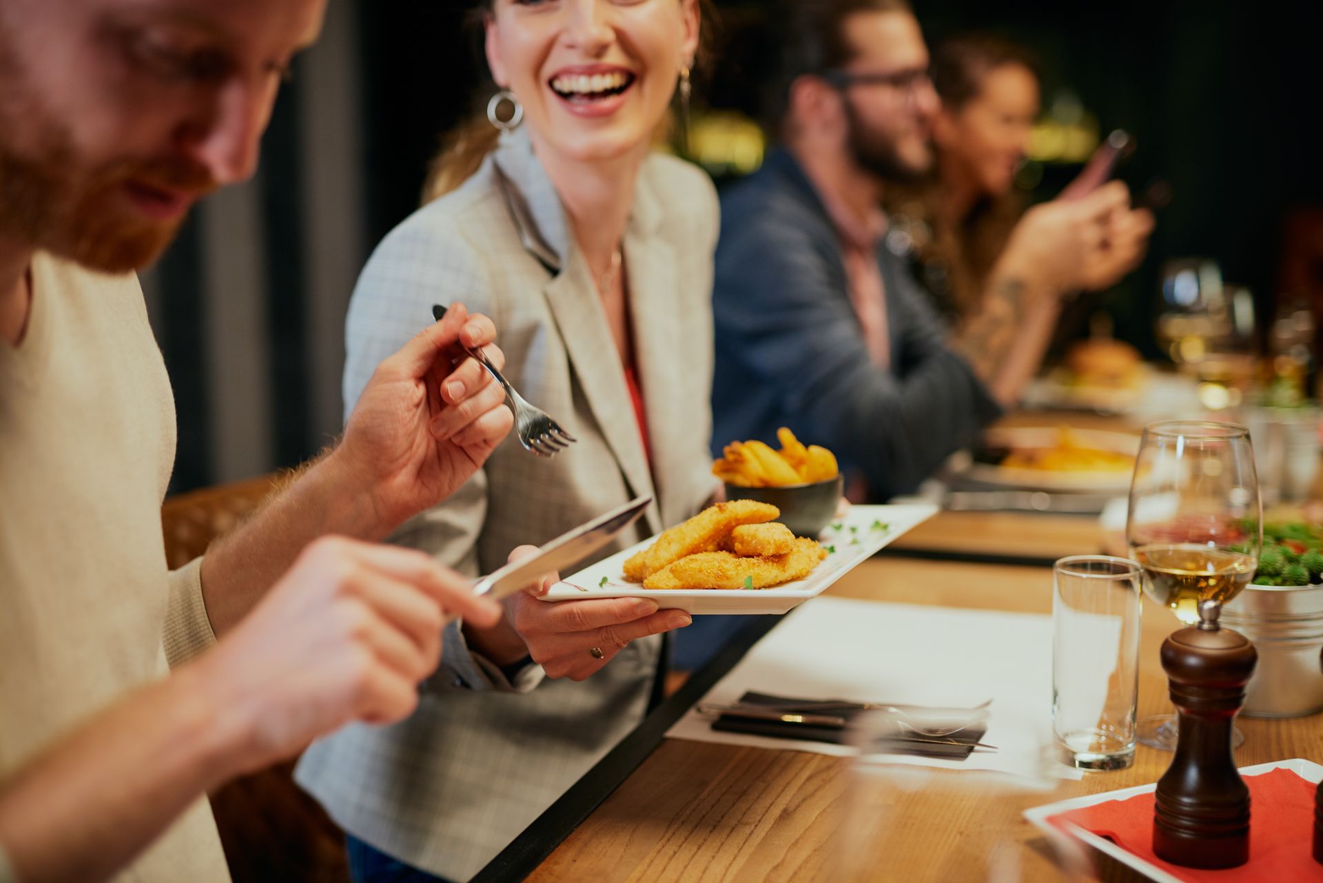 Un groupe de personnes rient et dînent ensemble à une table de restaurant, une assiette de friture circulant entre elles.