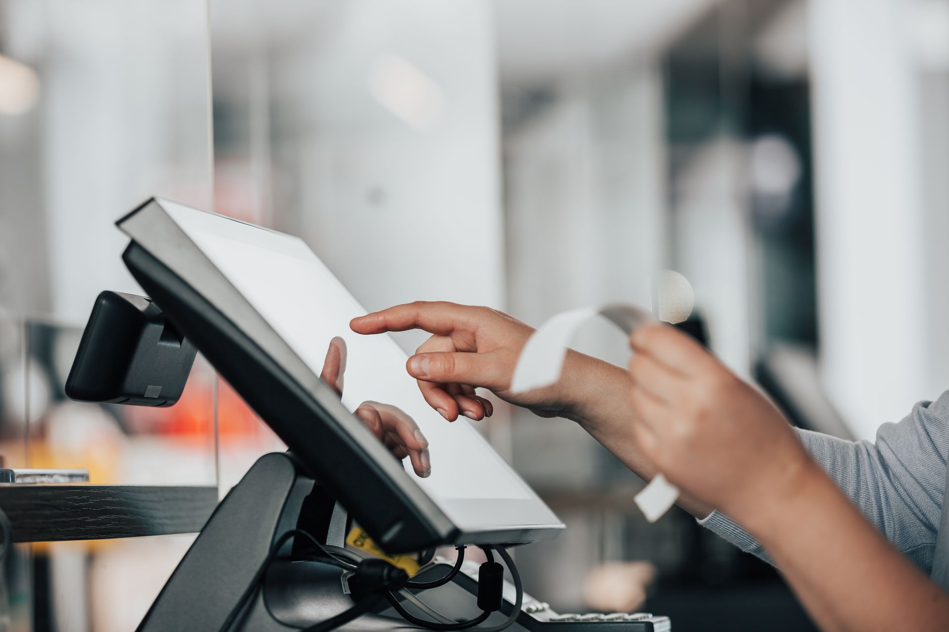 Les mains d'une personne manipulant un terminal de point de vente à écran tactile tout en tenant un reçu.