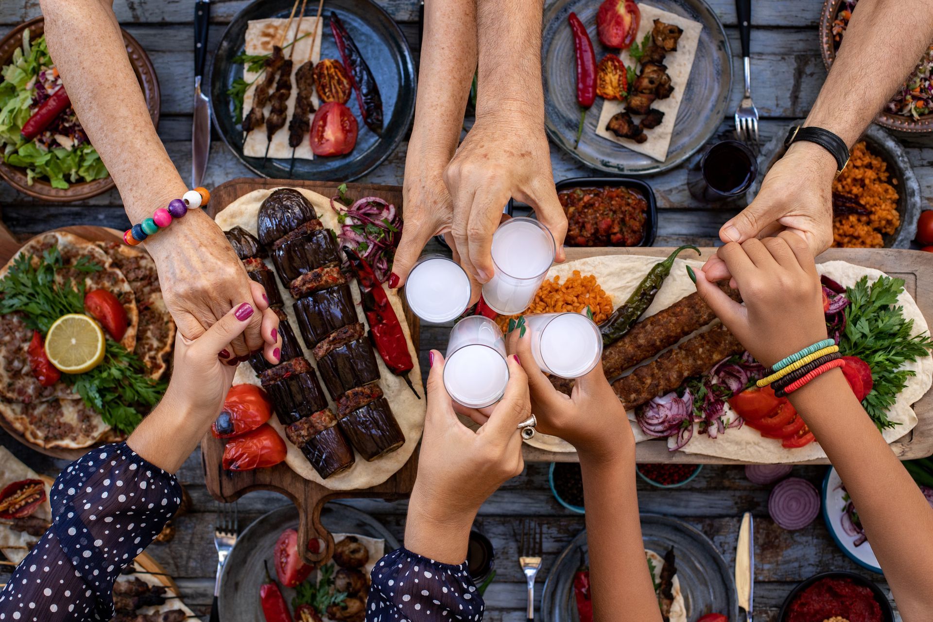 Quatre personnes trinquent avec des verres de raki autour d'une table garnie de divers mezze et kebabs turcs.