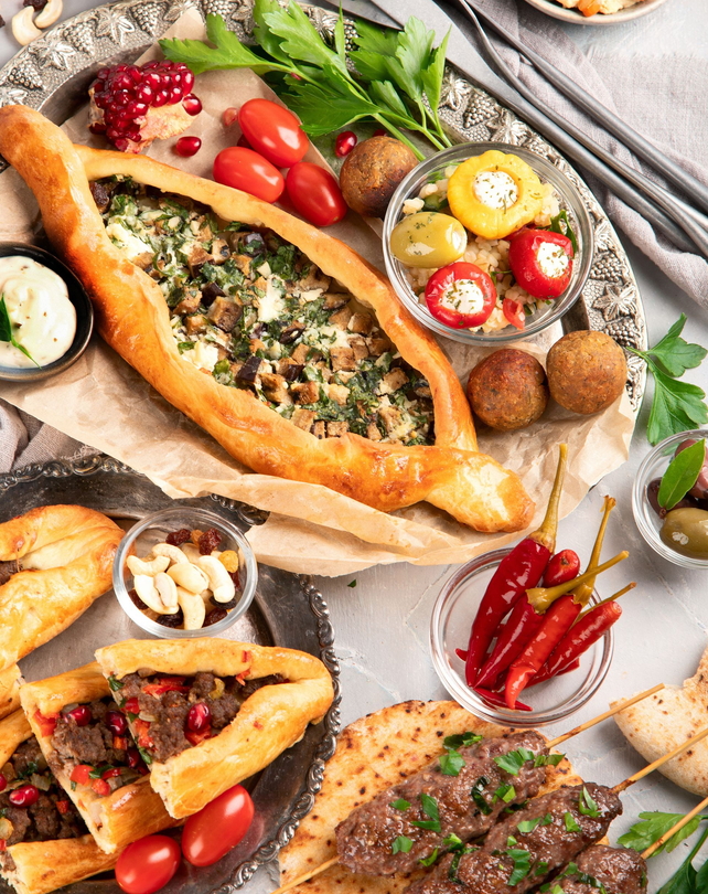 Un festin turc composé de pide, de brochettes, de falafels, de poivrons farcis et de graines de grenade disposés sur un plateau rustique.