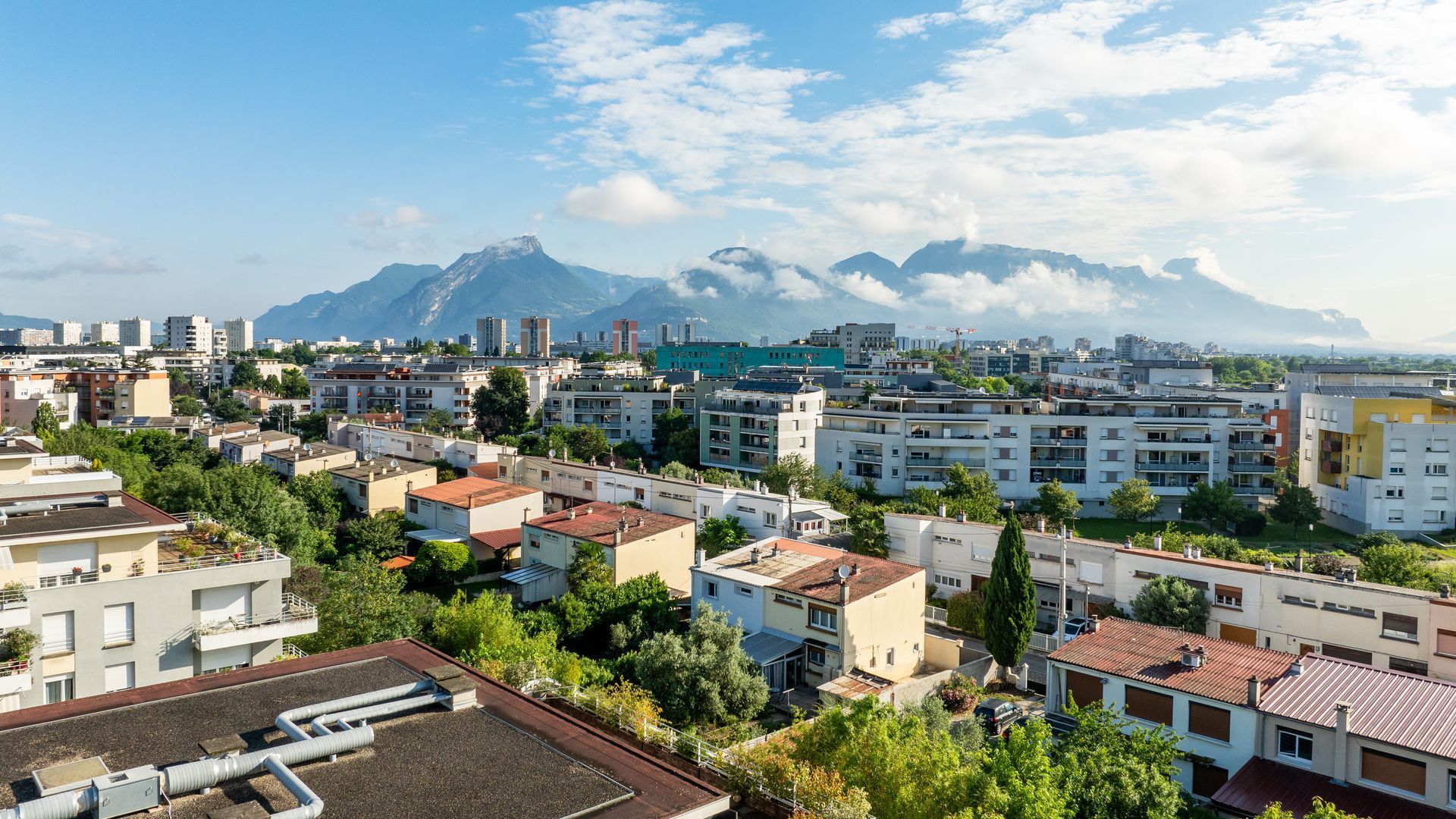 Quartier résidentiel dense, composé de maisons et d'immeubles d'appartements, sous un ciel montagneux et nuageux.