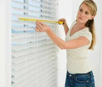 Uma mulher está medindo uma persiana com uma fita métrica.