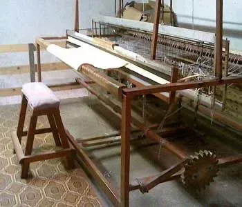 Um banco de madeira está ao lado de um tear em uma sala.