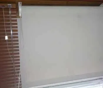 Uma persiana branca está pendurada em uma janela com persianas.