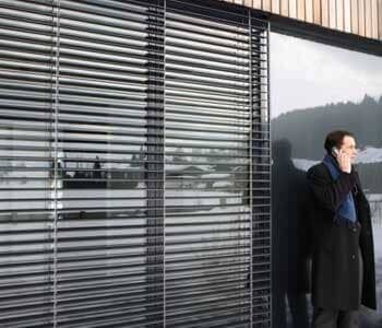 Um homem está parado em frente a uma janela falando ao celular.