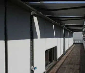 Há uma longa passarela entre dois prédios com persianas nas janelas.