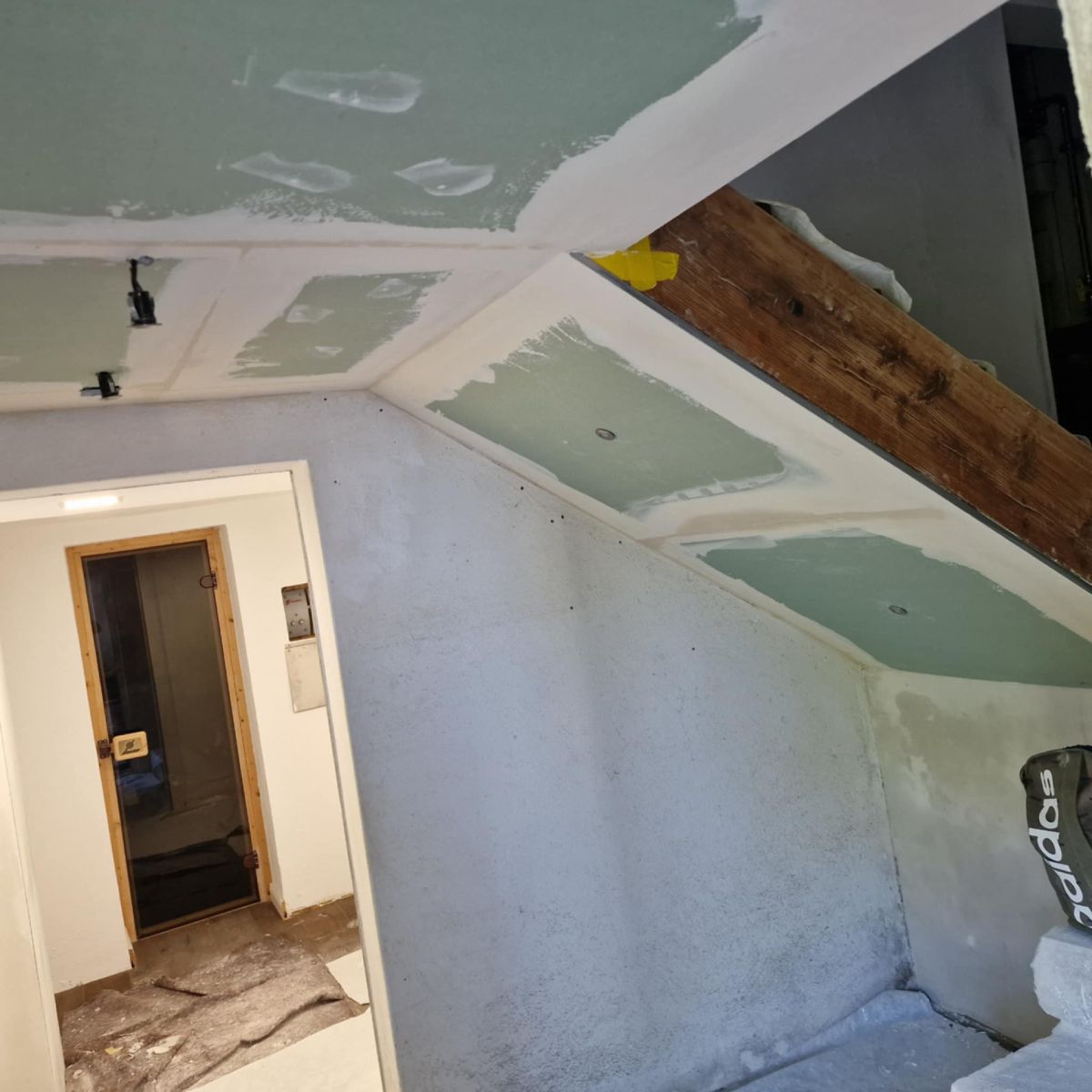 Baustelle: Trockenbaudecken- und Wandmontage in einem Dachzimmer mit sichtbaren Holzbalken.