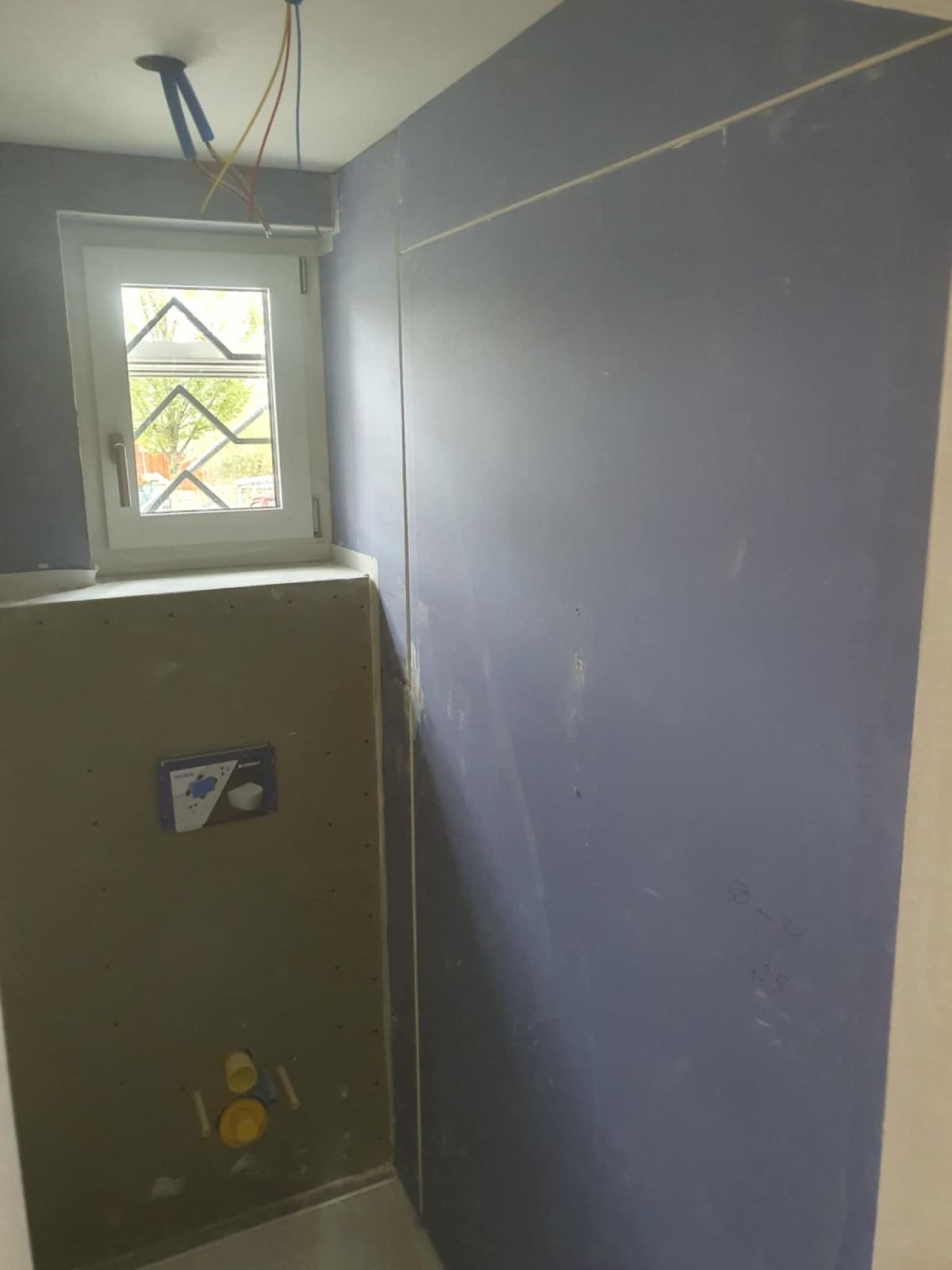 Badezimmer mit blauer Wand, Fenster, Toilettenarmatur und freiliegenden Rohren.