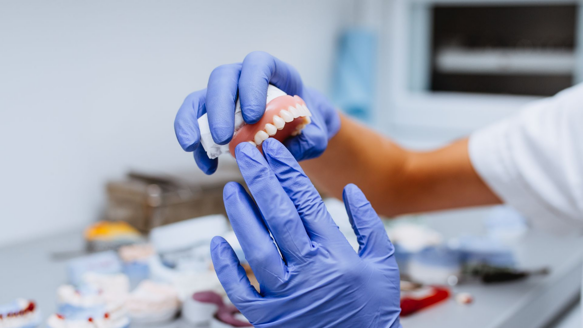 Des mains gantées tiennent un modèle dentaire avec un appareil orthodontique dans un espace de travail clinique