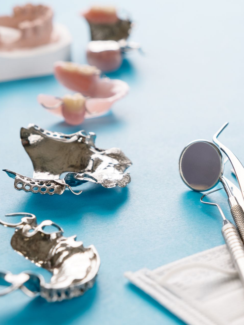Moules et instruments dentaires sur une surface bleue, avec un modèle rose et un miroir à côté.