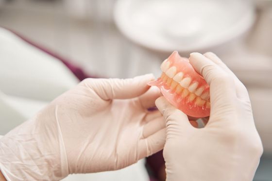 Des mains gantées tiennent un dentier dans un cabinet dentaire