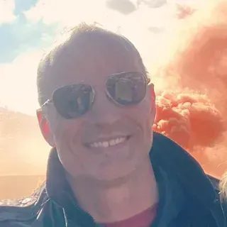 Un hombre que lleva gafas de sol sonríe frente a un cielo nublado.
