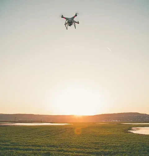 Un dron vuela sobre un campo de hierba al atardecer.