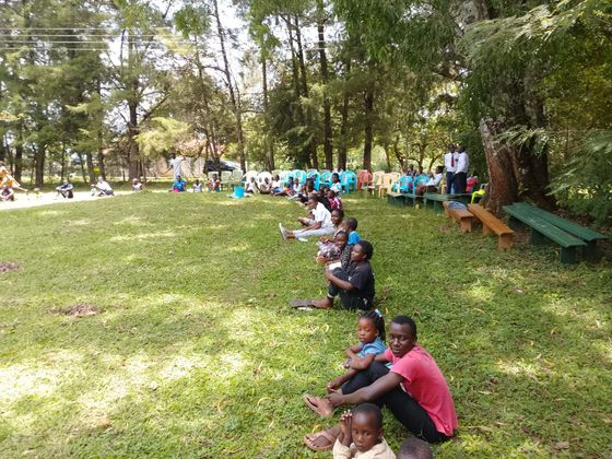 Children sitting in a circle outdoors, reaching toward the center on dry ground.