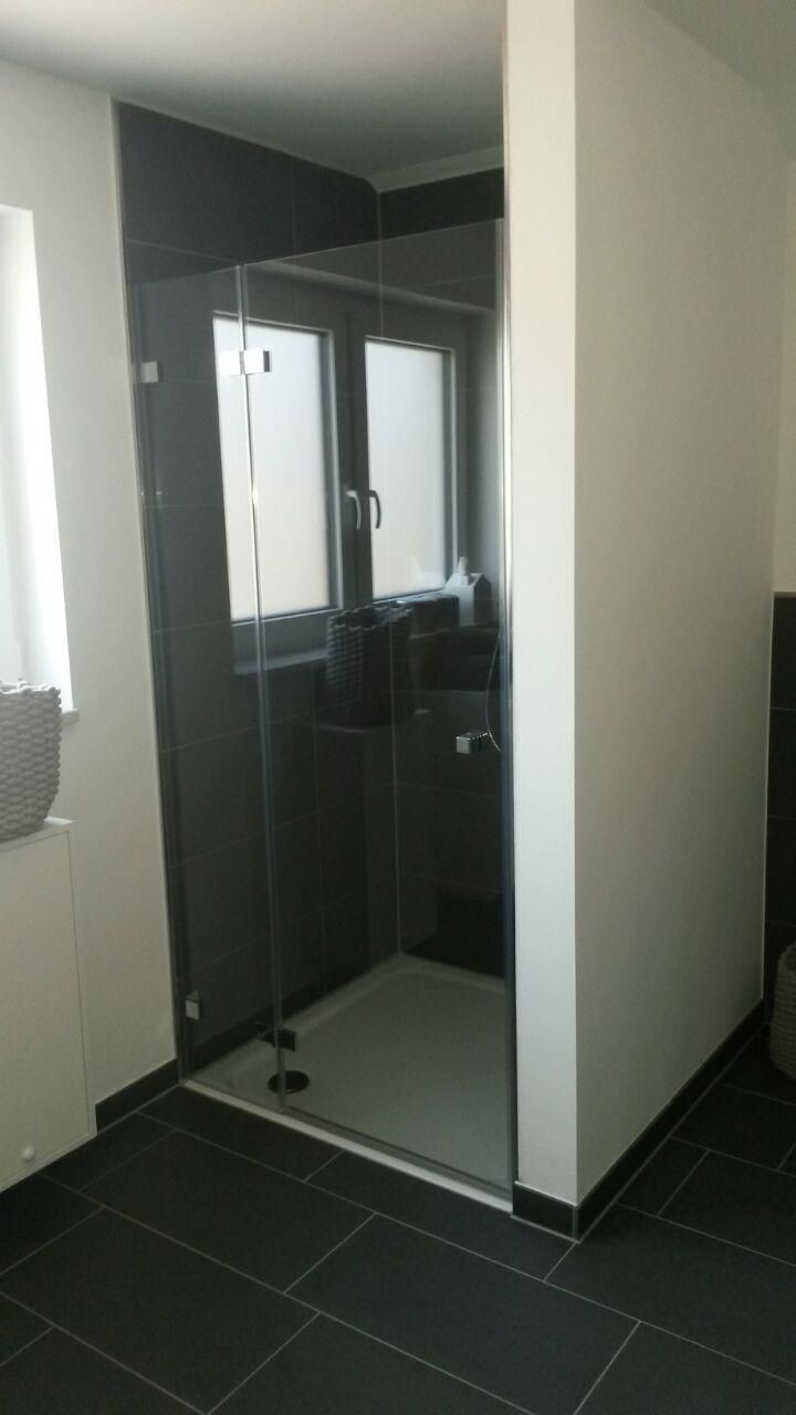 Ein Badezimmer mit einer Glasduschtür und einem Fenster.