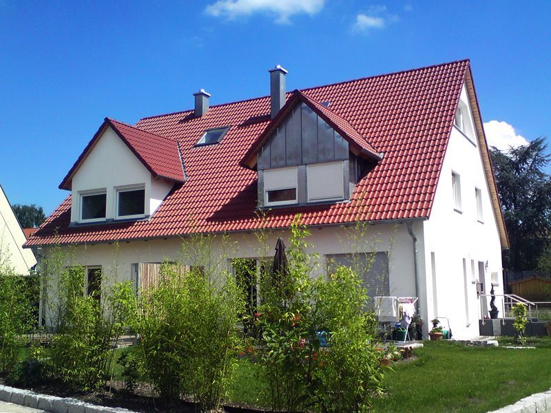 Großes Haus mit rotem Schrägdach, weißer Fassade und Garten