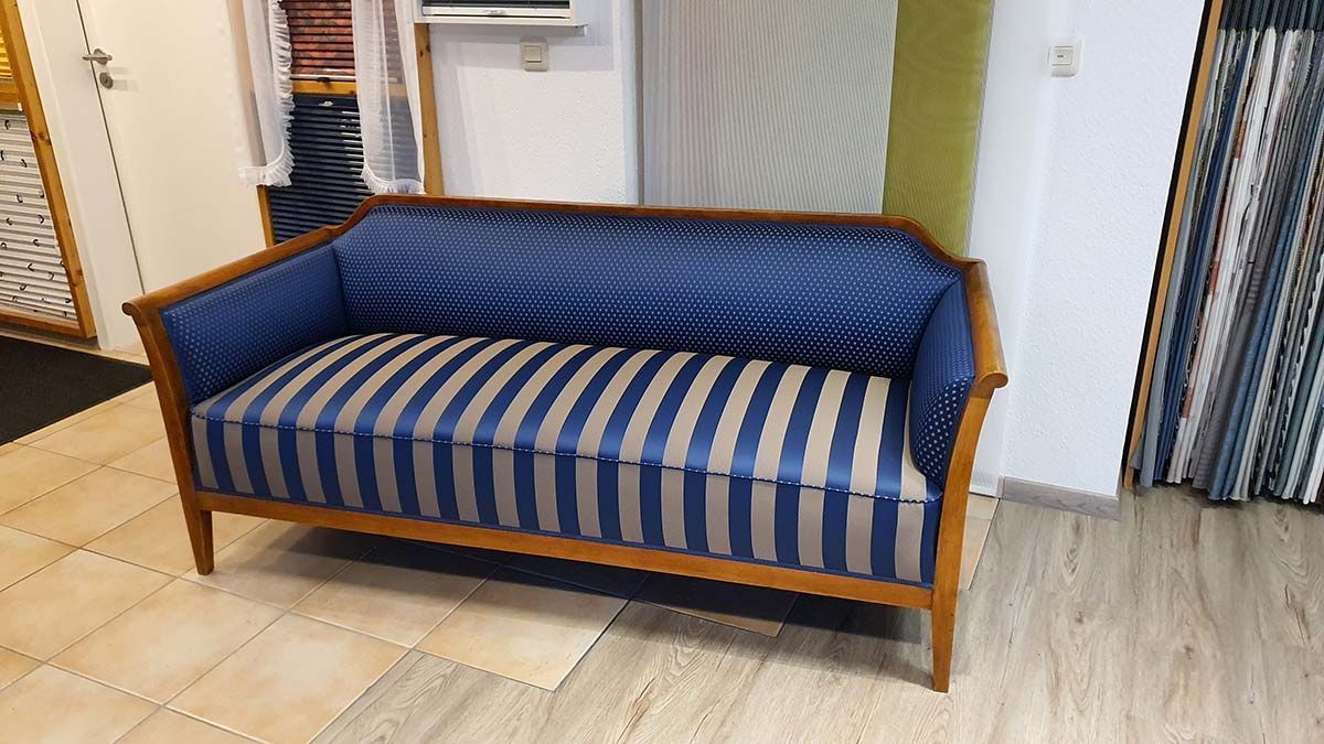 In einem Zimmer steht ein blau-weiß gestreiftes Sofa auf einem Holzboden.