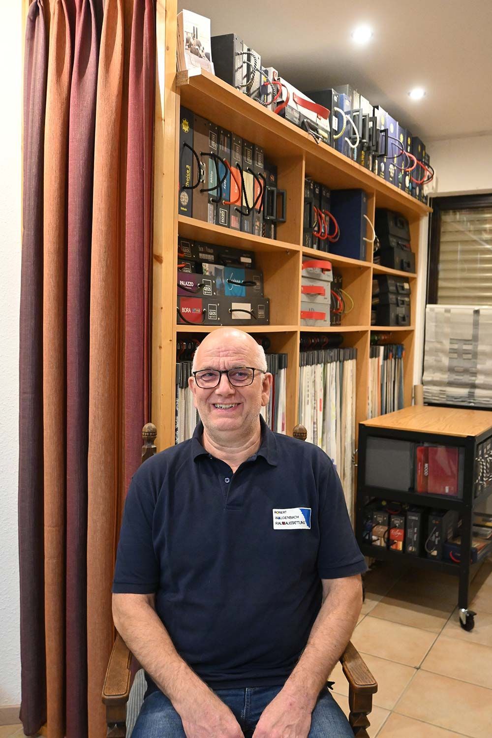 Ein Mann sitzt auf einem Stuhl vor einem Bücherregal.