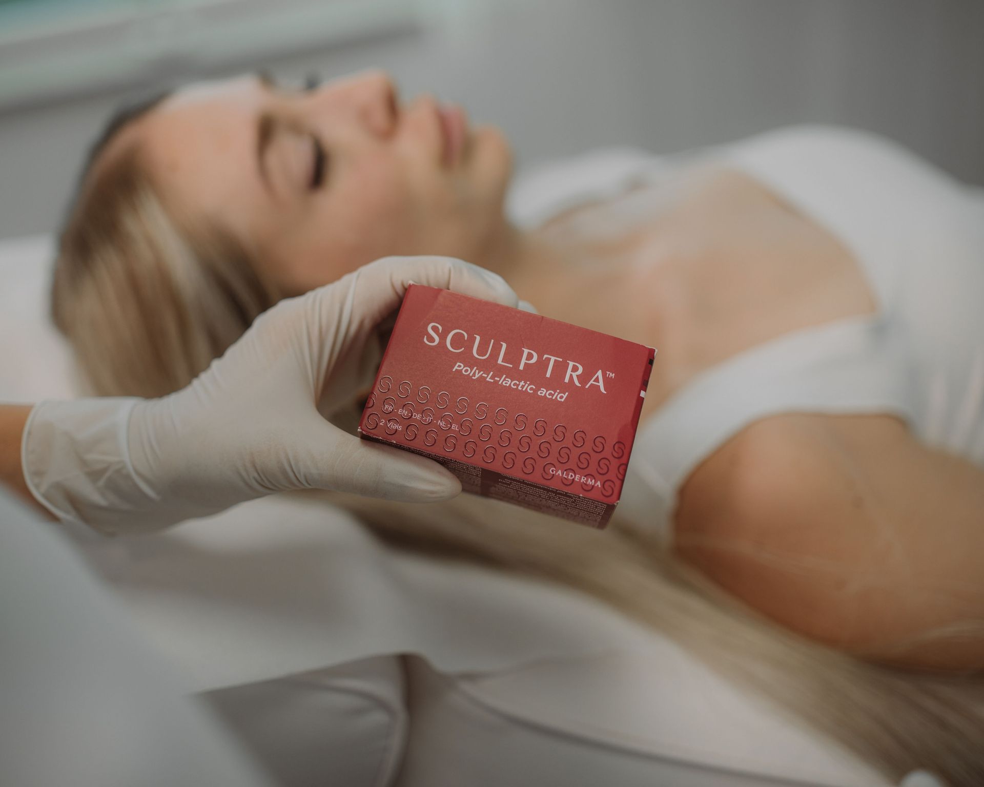 Hand mit weißem Handschuh hält eine rote Verpackung mit der Aufschrift 'SCULPTRA Poly-L-lactic acid'