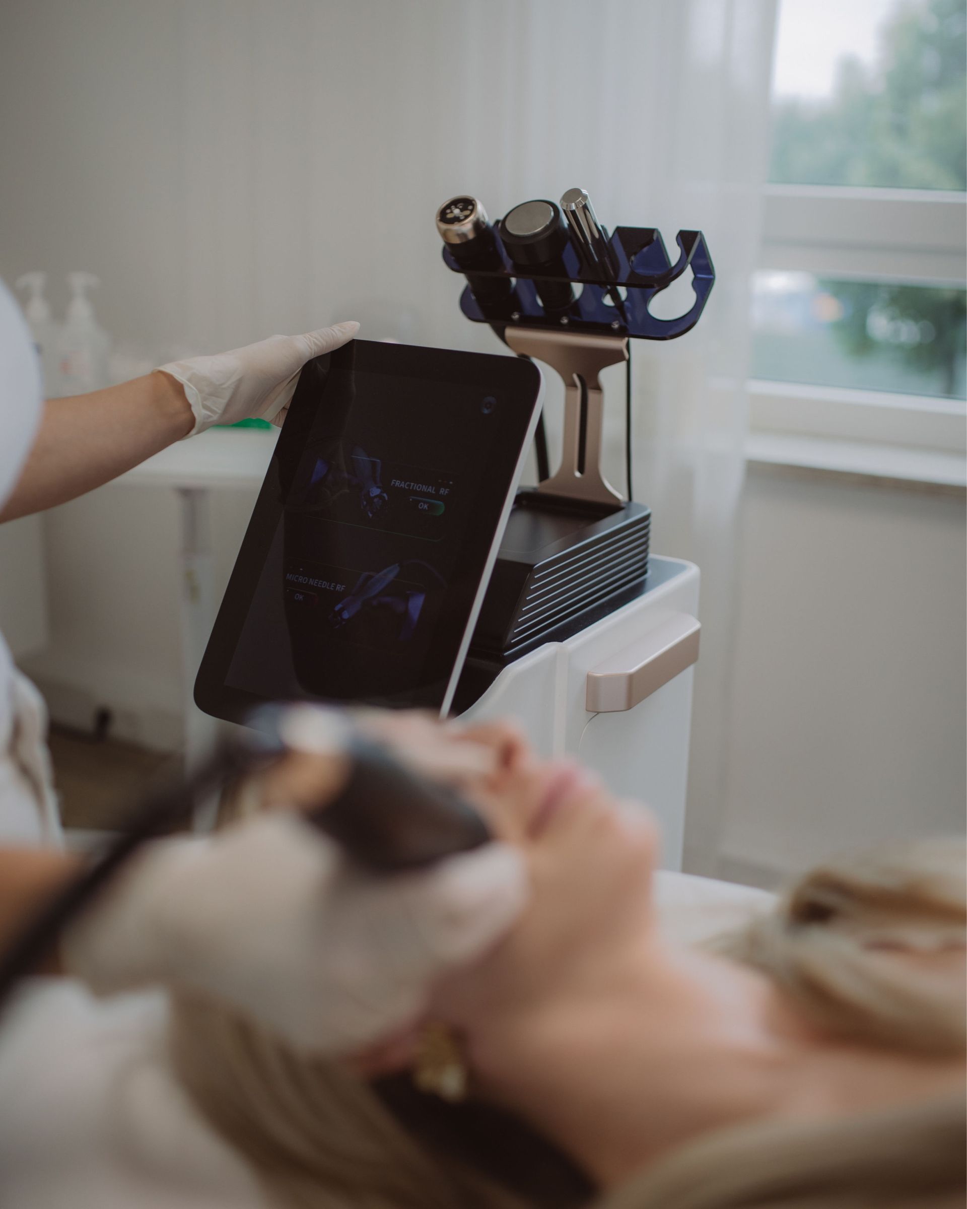 Kosmetikerin hält Gerät mit Bildschirm über liegende Frau während Gesichtsbehandlung im Behandlungsraum