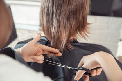 En una peluquería, un estilista utiliza tijeras de entresacar para recortar el cabello de una persona.