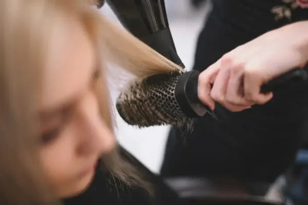 Un peluquero seca el cabello rubio de una clienta con un cepillo redondo en un salón.