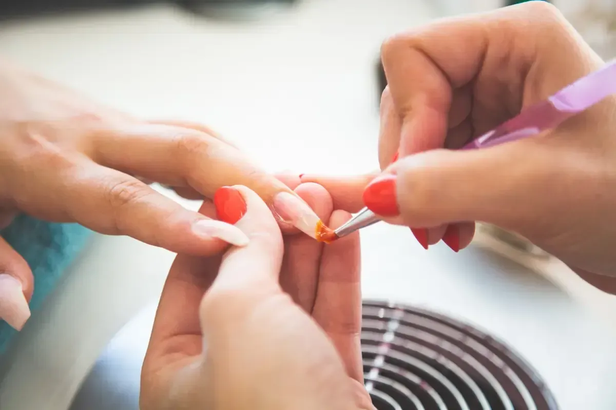 Manicurista aplicando esmalte de uñas a la uña de una clienta en un salón.