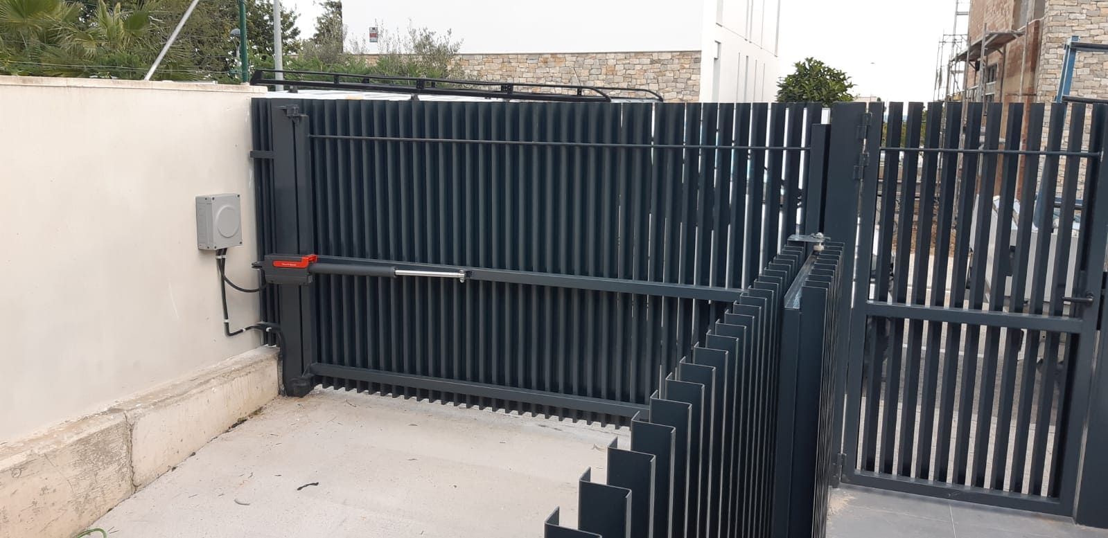 Una puerta de metal oscuro con barras verticales y abridor automático que conduce a un camino de entrada.